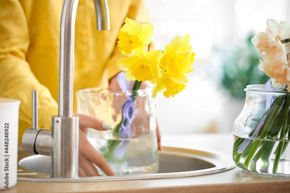 年轻女子在家里的水槽里往装有水仙花的花瓶里注水