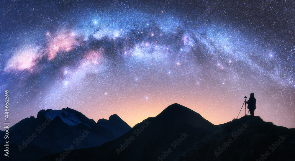 星夜山上的拱形银河和摄影师。手持三脚架的人的剪影是