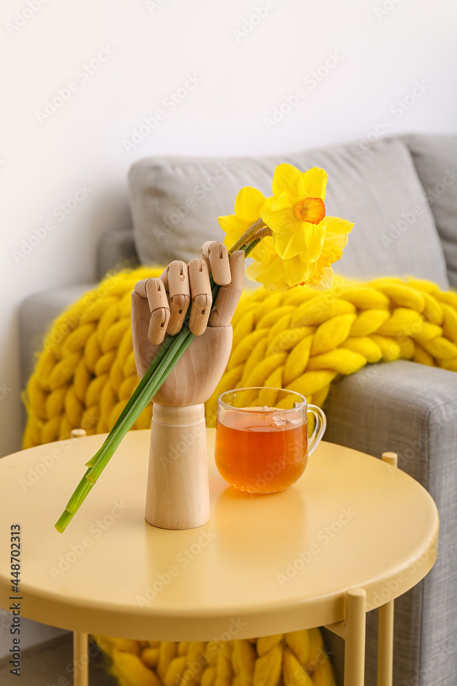 室内桌子上拿着水仙花和一杯茶的人形手