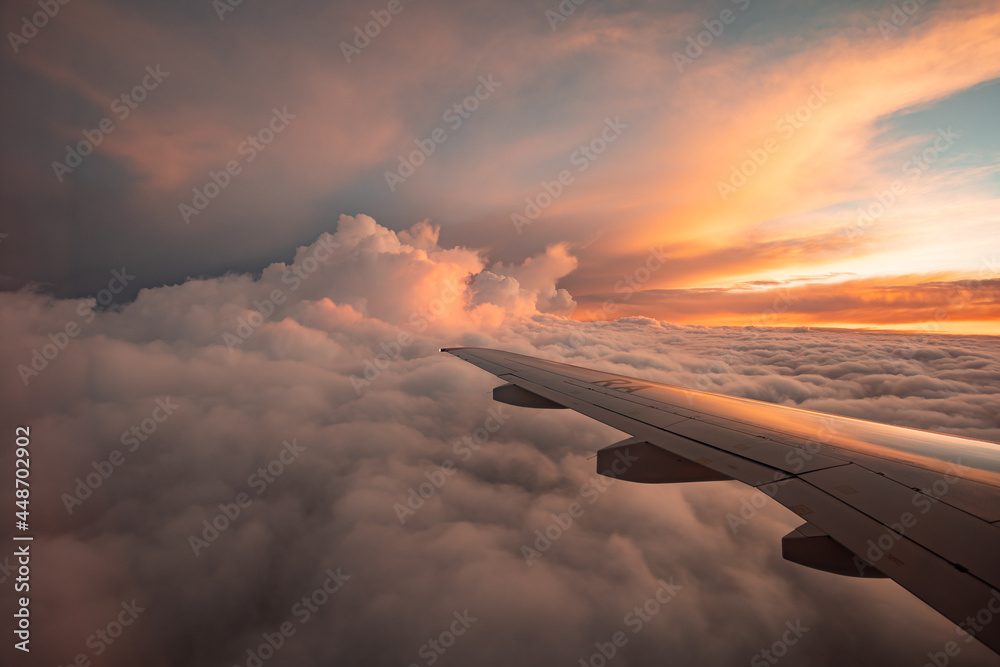 从飞机窗户到云层和日落的景色。飞机机翼在厚厚的粉红色和橙色上方