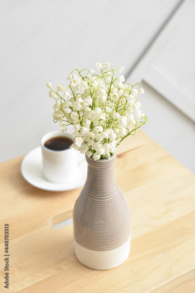 浅墙上的桌子上放着铃兰花和一杯咖啡的花瓶