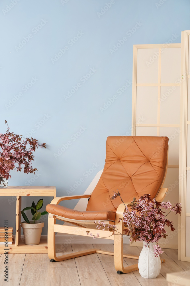 现代扶手椅和花瓶，彩色墙附近有开花的树枝