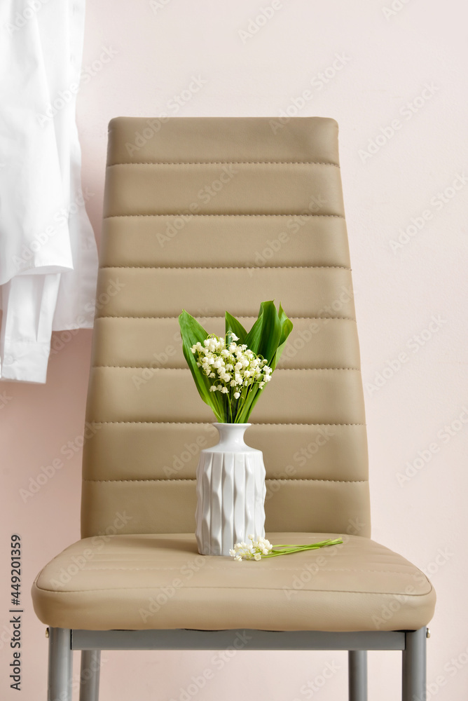 靠近彩色墙的椅子上放着铃兰花的花瓶