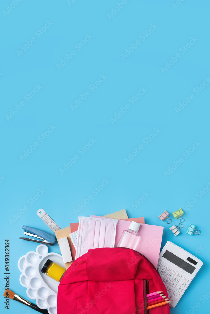 蓝色桌子背景上有文具的粉红色背包。