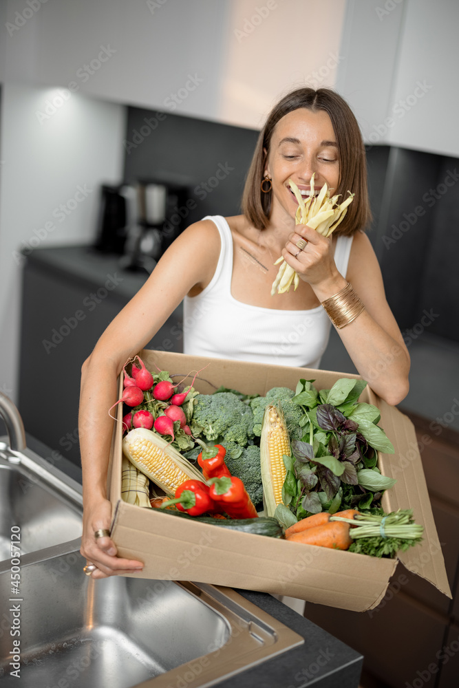 年轻女子拿着厨房纸板箱里的新鲜蔬菜。网上送餐和买菜