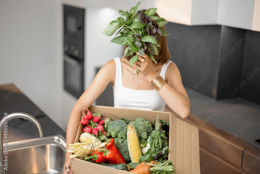 年轻女子拿着厨房纸板箱里的新鲜蔬菜。网上送餐和买菜