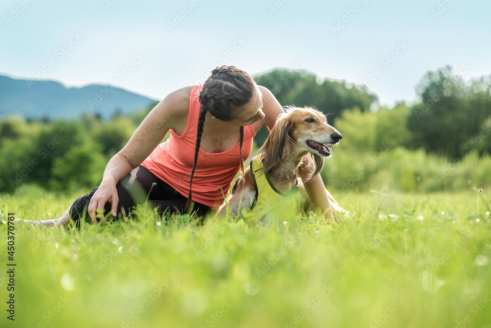 Woman and dog on field under golden sunset sky in evening time. Outdoor running. Athletic young man 