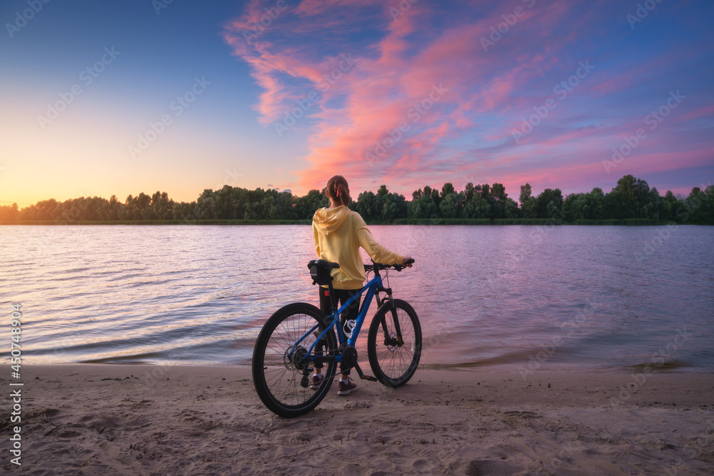 夏天日落时，一个骑着山地自行车的女人在河边。年轻女孩的风景，自行车，