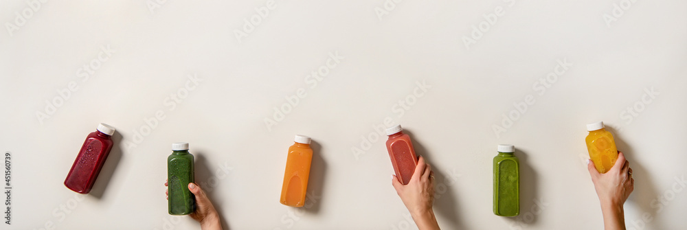 Flat-lay of human hands holding fresh juices in bottles