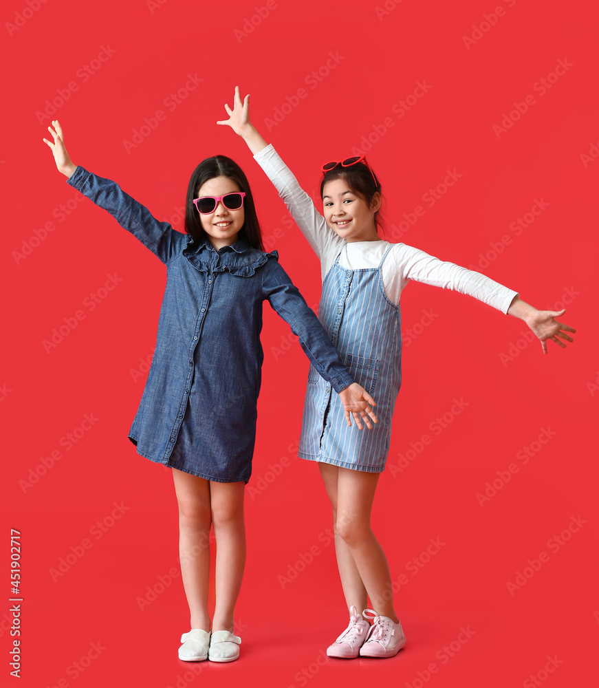 Stylish little sisters on color background
