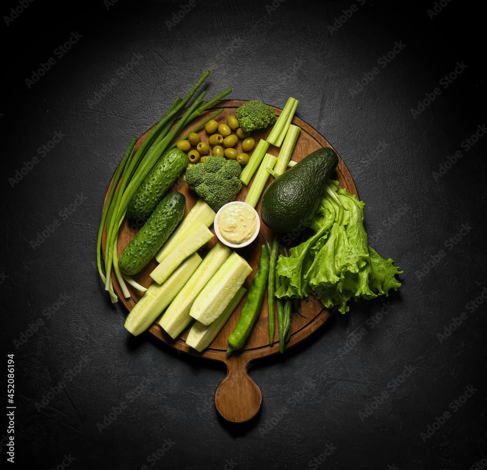 不同绿色蔬菜板和深色背景酱汁碗