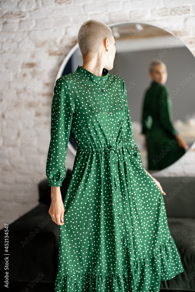 穿着绿色连衣裙的时髦女人看着镜子里的自己，准备出门。女性风格