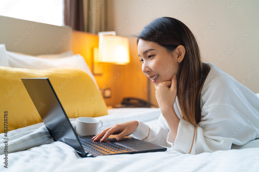 亚洲女子穿着浴袍，早上喝咖啡时用笔记本电脑进行视频通话的照片