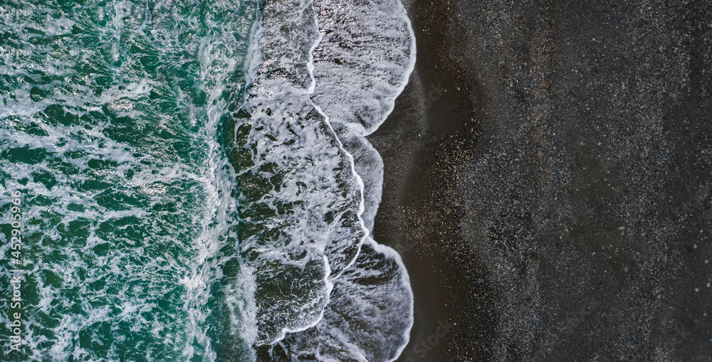 海浪和黑沙的戏剧性纹理的海岸，无人机视角