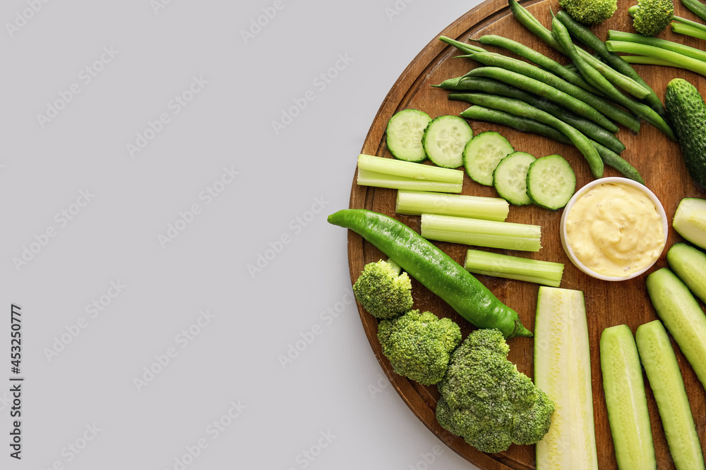 不同绿色蔬菜的木板和浅色背景的酱汁碗