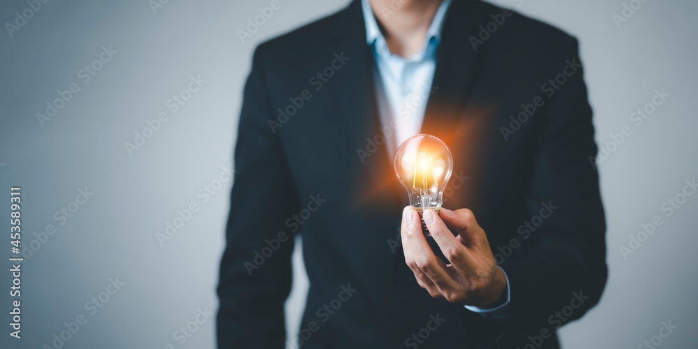 商人手持灯泡，带线路连接，在桌子上工作，创意与创新