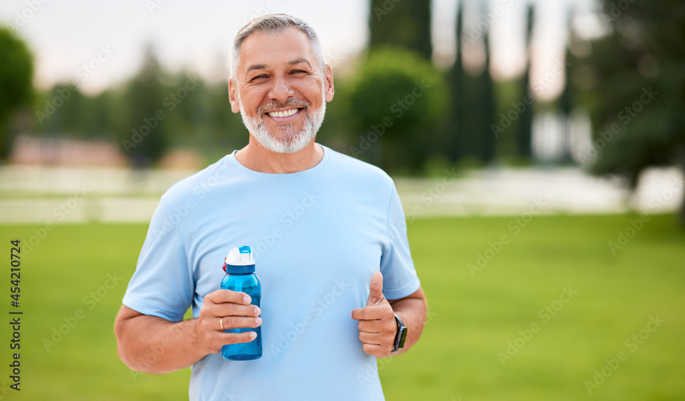 快乐、积极、成熟的男人，笑容灿烂，在城市公园里运动时拿着水瓶