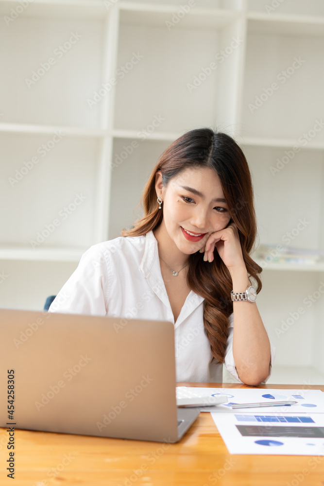 年轻的亚洲商务女性在办公室用笔记本电脑工作，桌上放着文件