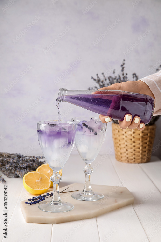 Woman preparing fresh cocktail with lavender at table, closeup
