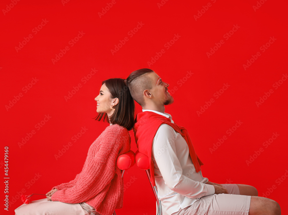 时尚的年轻情侣坐在红色背景的椅子上