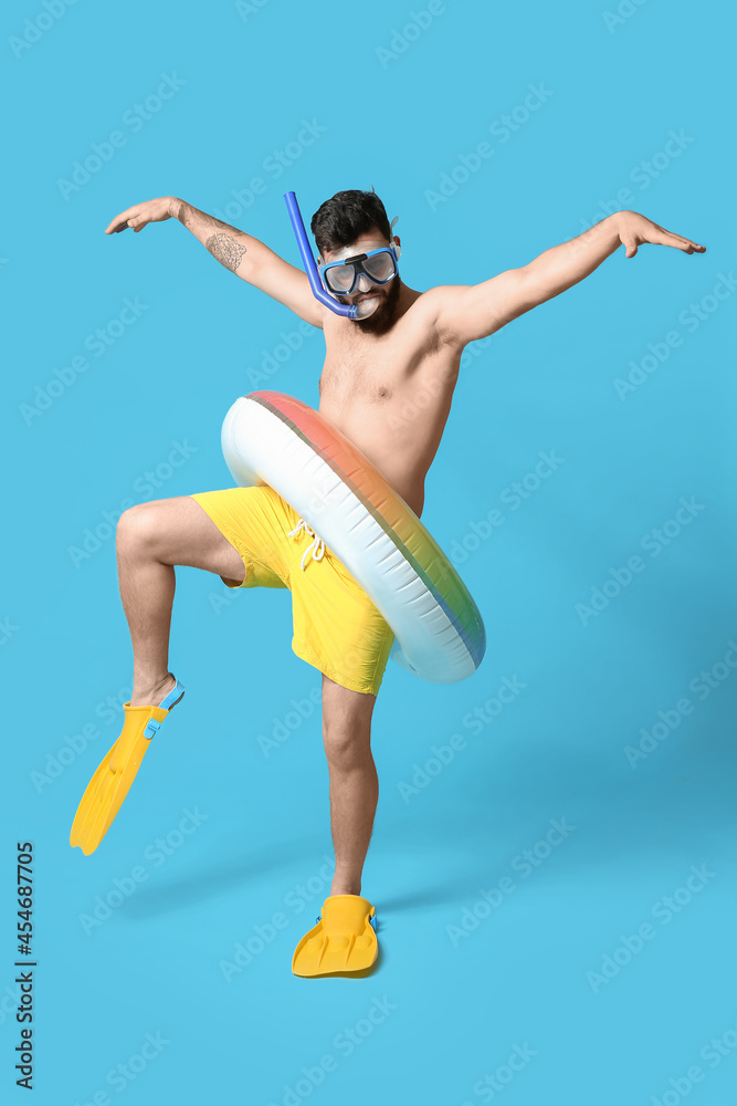 Funny young man with inflatable ring, paddles and snorkeling mask on color background