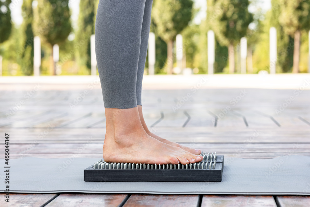 Yogi woman in gray pants standing barefoot on a wooden board with nails during outdoor yoga class