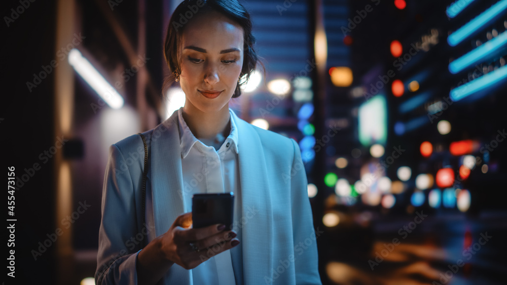 美丽的年轻女子使用智能手机穿过充满霓虹灯的夜城街道。波特拉伊
