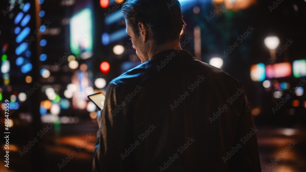 下面是一张英俊男子使用智能手机在霓虹灯下的现代城市街道上行走的照片