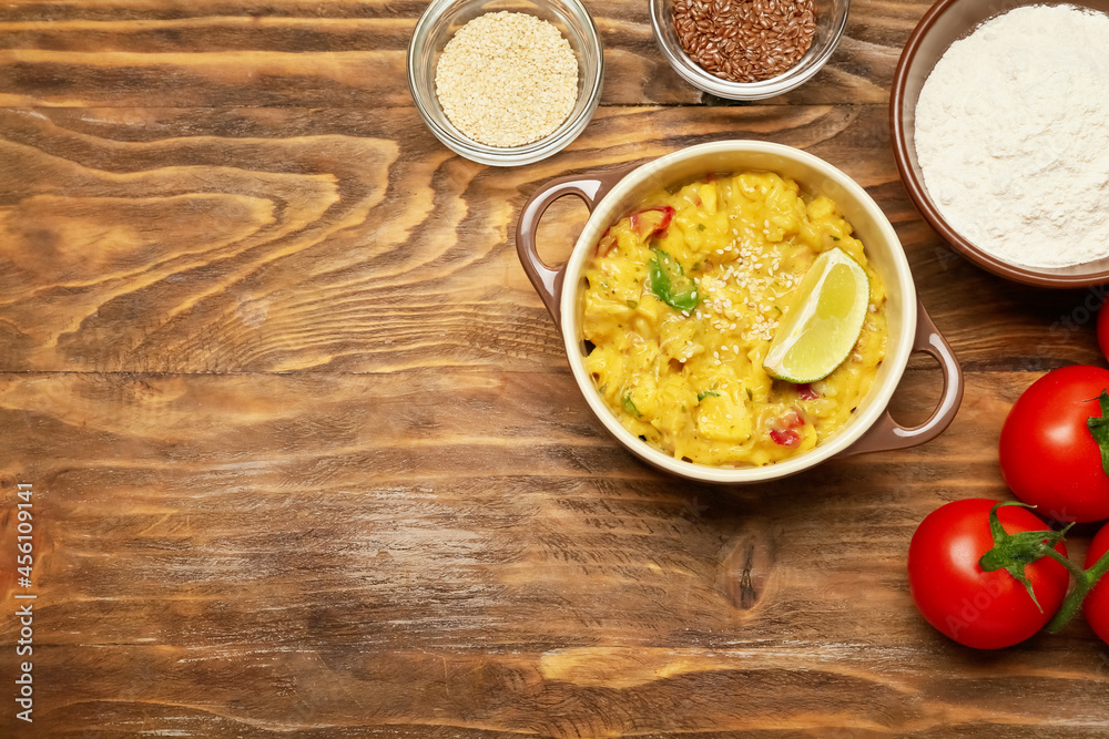 Pot of tasty chicken curry and ingredients on wooden background