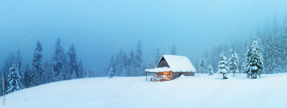 梦幻般的冬季景观全景，雪地森林中有发光的木屋。Carpath的舒适房子