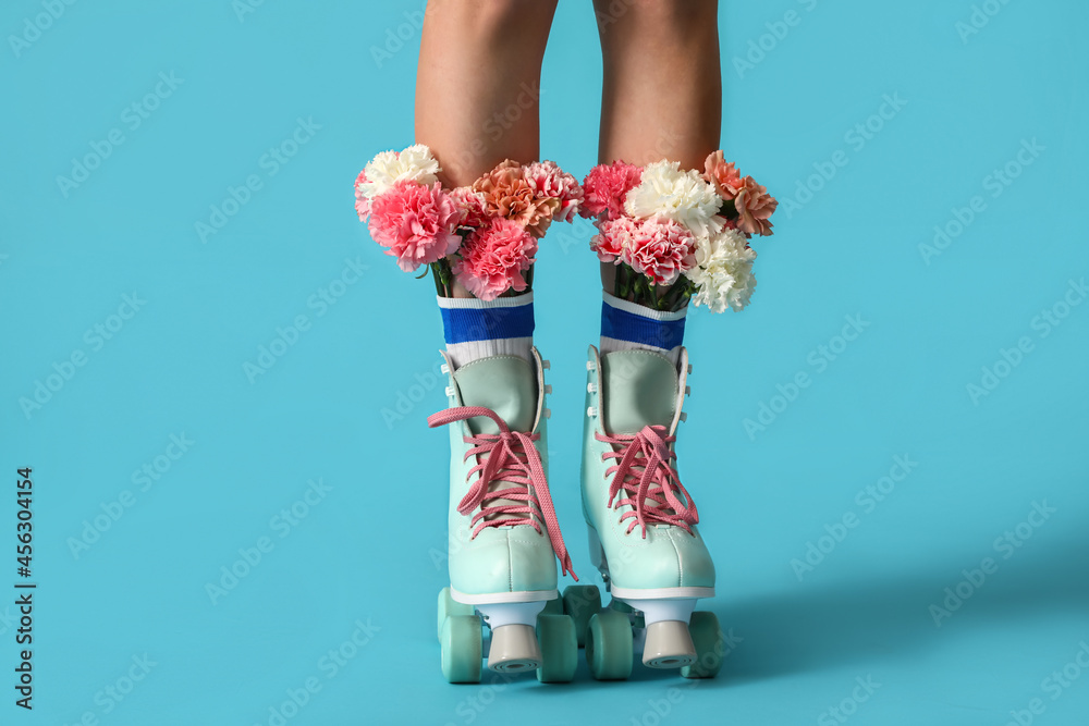 Legs of young woman in roller skates with flowers on color background