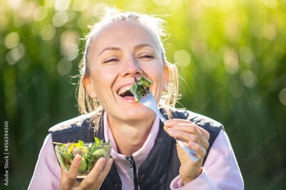 美丽的高加索女人在绿色自然背景下吃沙拉