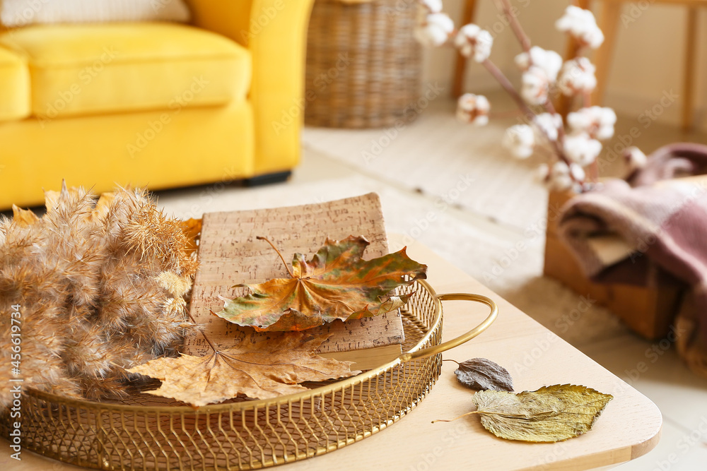 Tray with autumn leaves, reed branches and book on table in interior of living room, closeup