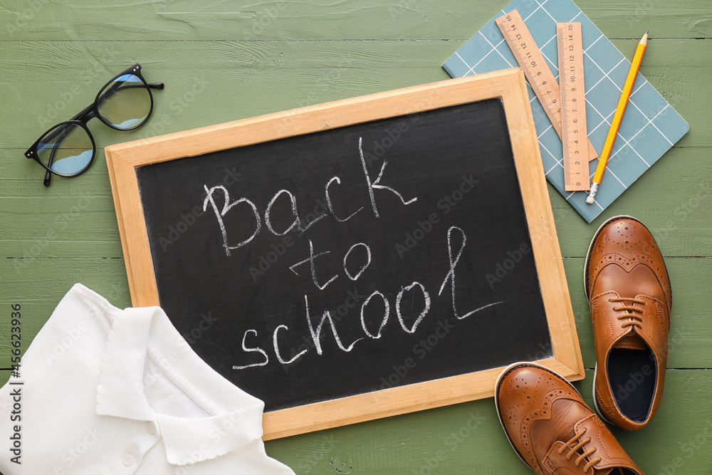 Chalkboard with text BACK TO SCHOOL, uniform, shoes, stationery and eyeglasses on color wooden backg