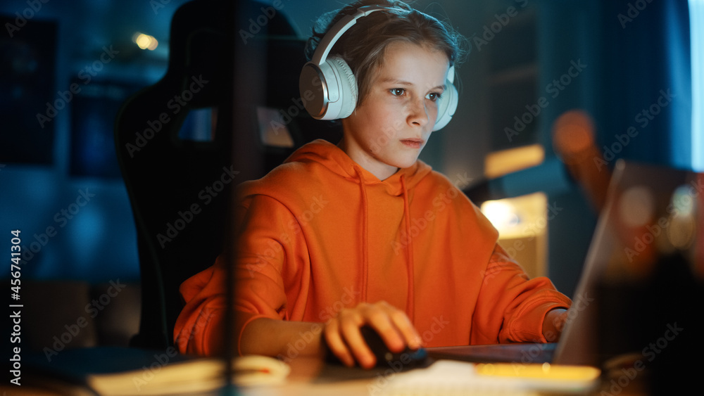 兴奋的年轻男孩戴着耳机在家里舒适的暗室里用笔记本电脑玩电子游戏。哈