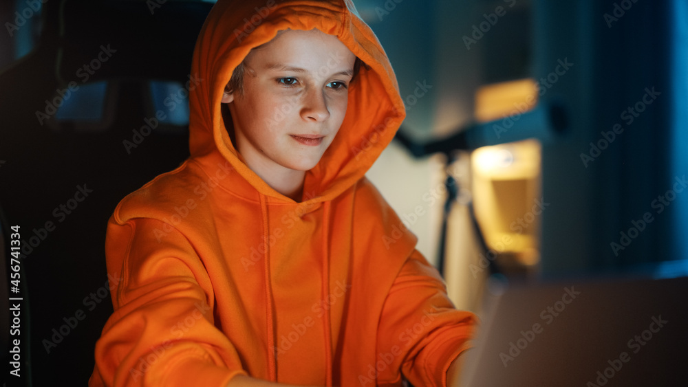 可爱的连帽衫男孩在家里舒适的暗室里使用笔记本电脑。快乐的青少年浏览