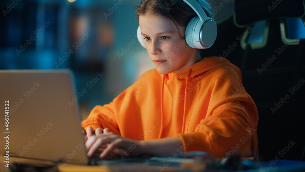 戴着耳机的聪明男孩在家里黑暗舒适的房间里使用笔记本电脑。快乐的青少年眉毛