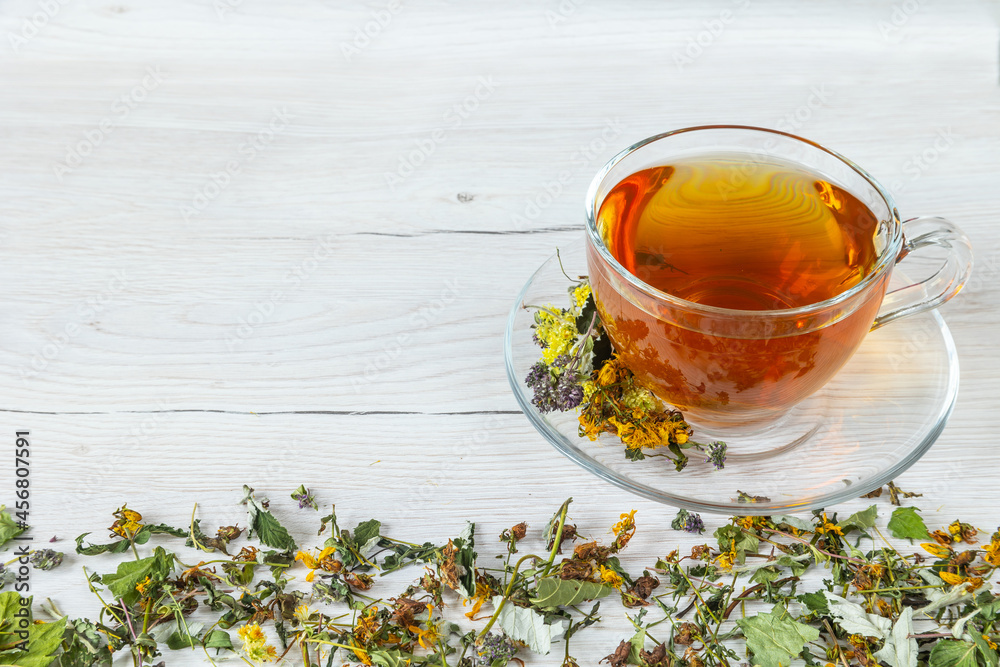 Cup of herbal tea with natural dried herbs on white wooden background.