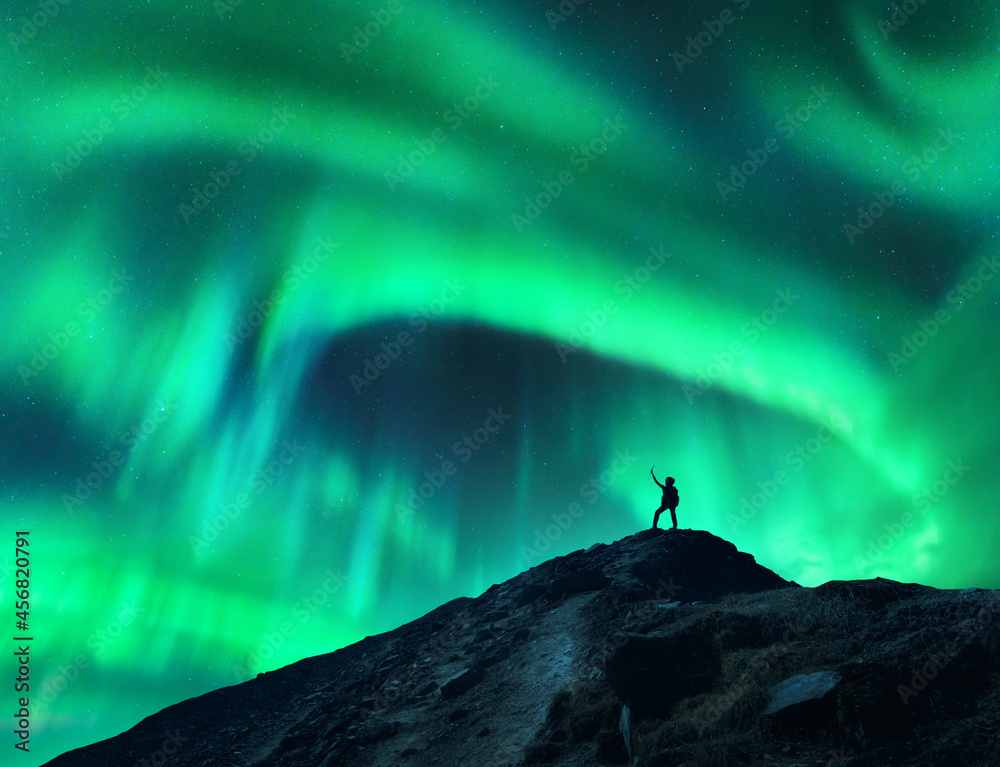 北极光和山上举起双臂站着的女人的剪影。北极光