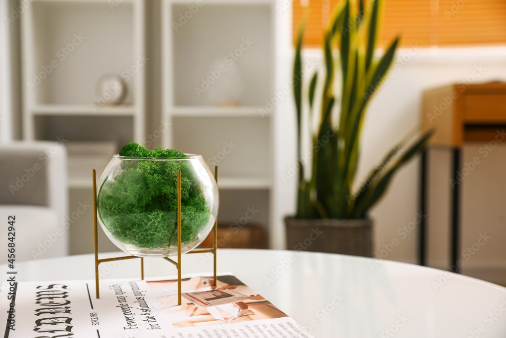 房间桌子上有装饰性绿苔和报纸的玻璃容器