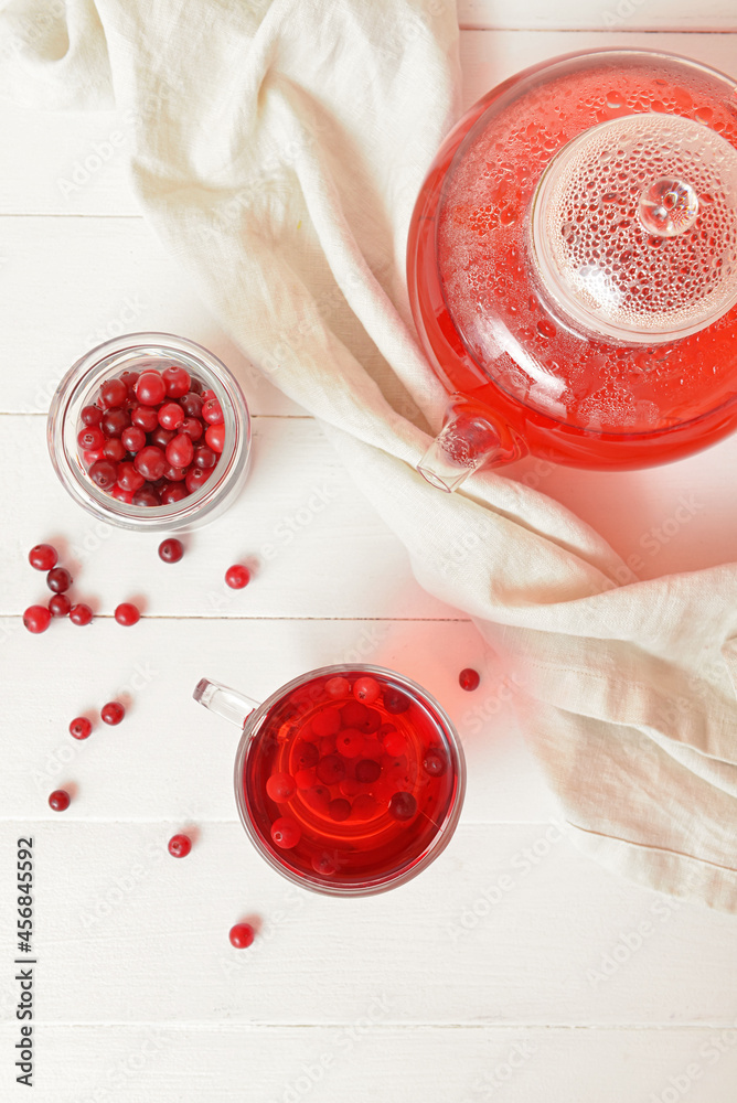 Cup and teapot of tasty tea with cranberry on light wooden background