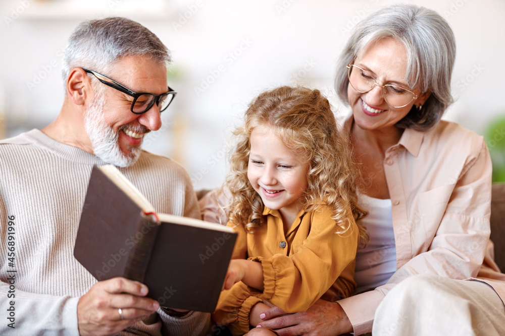 可爱的小女孩孙女和爷爷奶奶一起看书时面带微笑