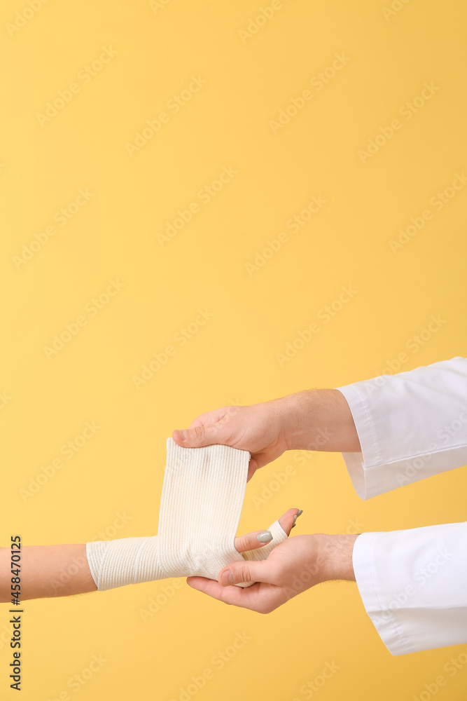 Doctor applying bandage onto hand of young woman on color background