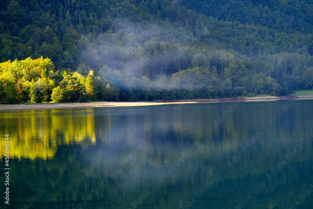 Lake Klöntal with little mist and reflections in calm water at a beautiful late summer morning. Phot