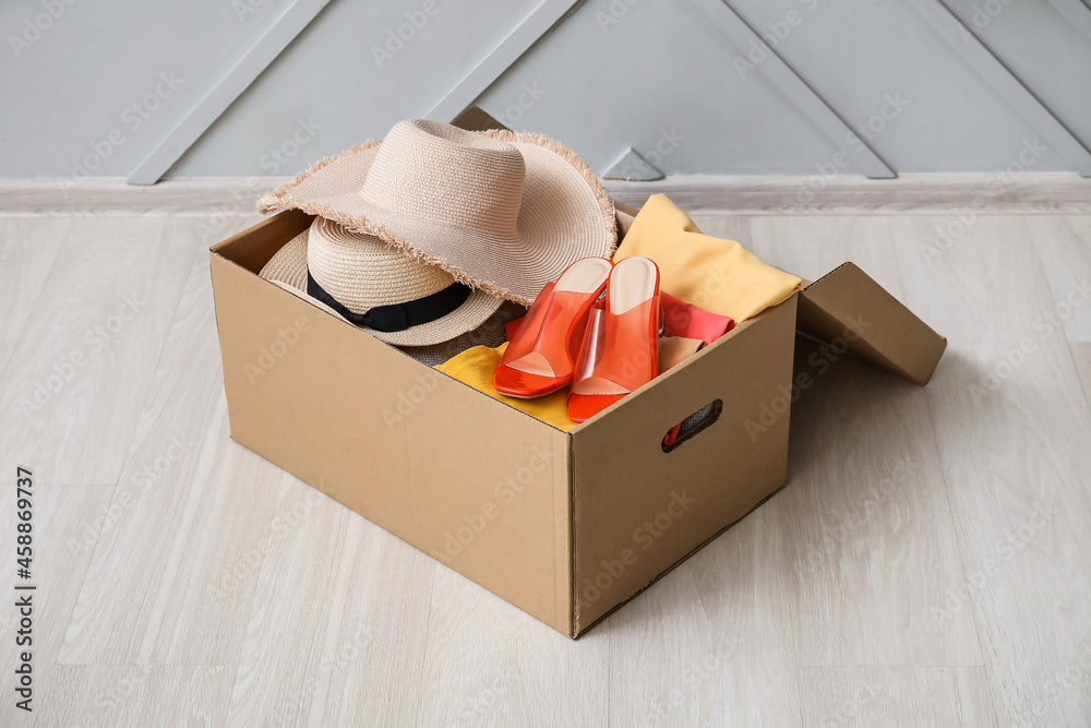 Wardrobe box with clothes, hat and shoes on wooden floor near light wall