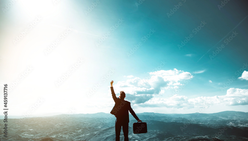 Silhouette of successful businessman keeping hands up hiking on the top of mountain - Celebrating su