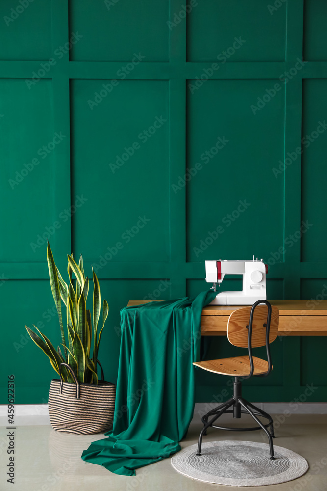 绿色墙壁附近有缝纫机、布料和室内植物的裁缝工作场所