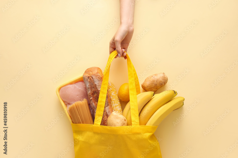 拿着黄色背景不同产品的环保袋的女人