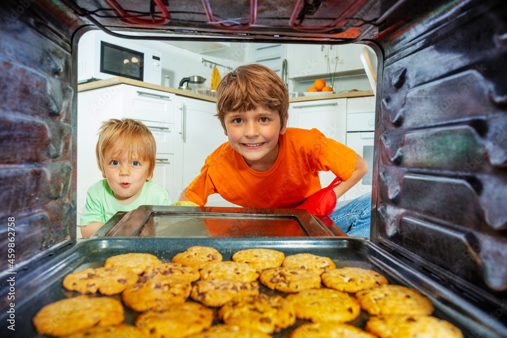 两个男孩打开烤箱门，看着新鲜的饼干