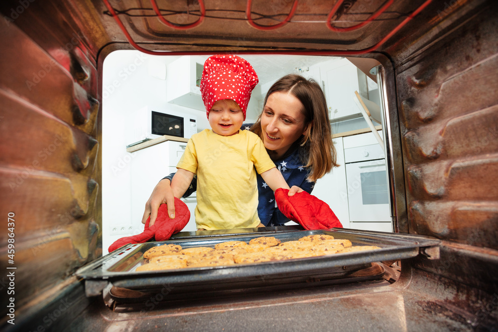戴厨师帽的妈妈和男孩从烤箱里拿饼干
